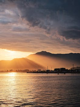 Breathtaking sunset over a coastal town silhouetted against majestic mountains and calm sea.