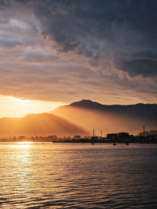 Free Breathtaking sunset over a coastal town silhouetted against majestic mountains and calm sea. Stock Photo
