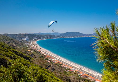 Free A breathtaking view of a paraglider over a beautiful Mediterranean beach with clear blue waters. Stock Photo