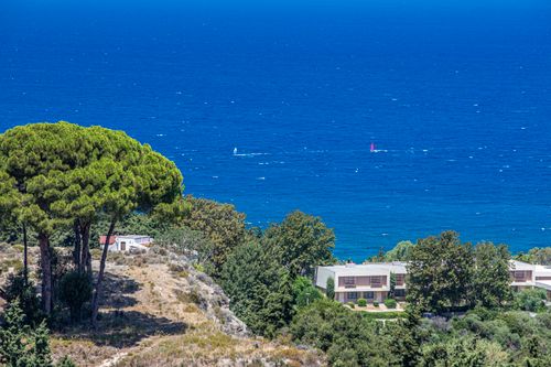 Free Scenic view of coastal houses with lush greenery overlooking the calm blue sea and windsurfers. Stock Photo