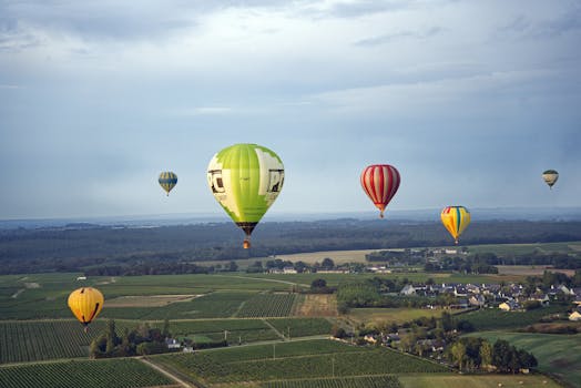 Hot air balloons soaring over verdant fields and distant villages under a broad blue sky.