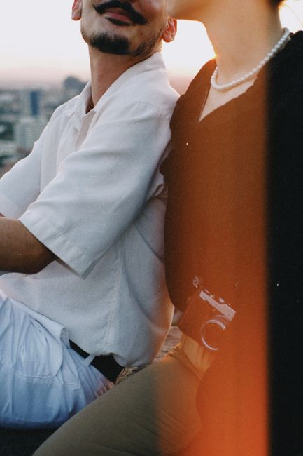 Close-up of a fashionable couple sitting together with a vintage camera at sunset.