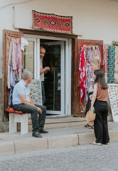 Free Customers interact at a traditional souvenir shop displaying vibrant textiles and trinkets. Stock Photo