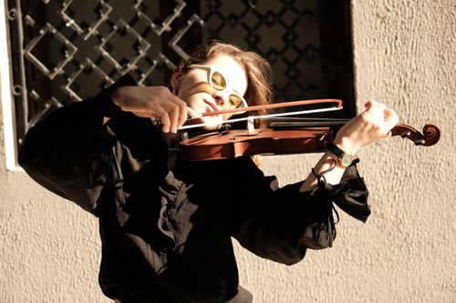 Free A woman in sunglasses plays a violin outdoors in bright sunlight, wearing black clothes. Stock Photo