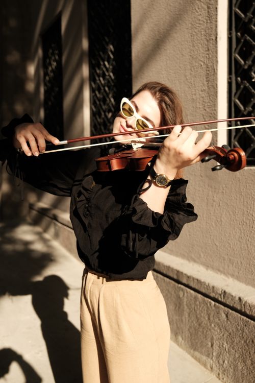 Free Stylish woman with sunglasses plays violin in an urban setting, bathed in sunlight. Stock Photo