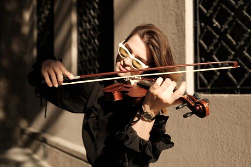 Free A woman in sunglasses plays the violin outdoors beside a sunlit wall. Stock Photo