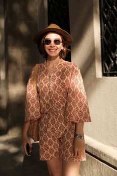 A cheerful woman wearing stylish summer attire and sunglasses on a sunny day outdoors.