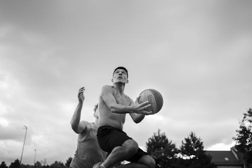 Black and White Photograph of Basketball Players against Clouded Sky