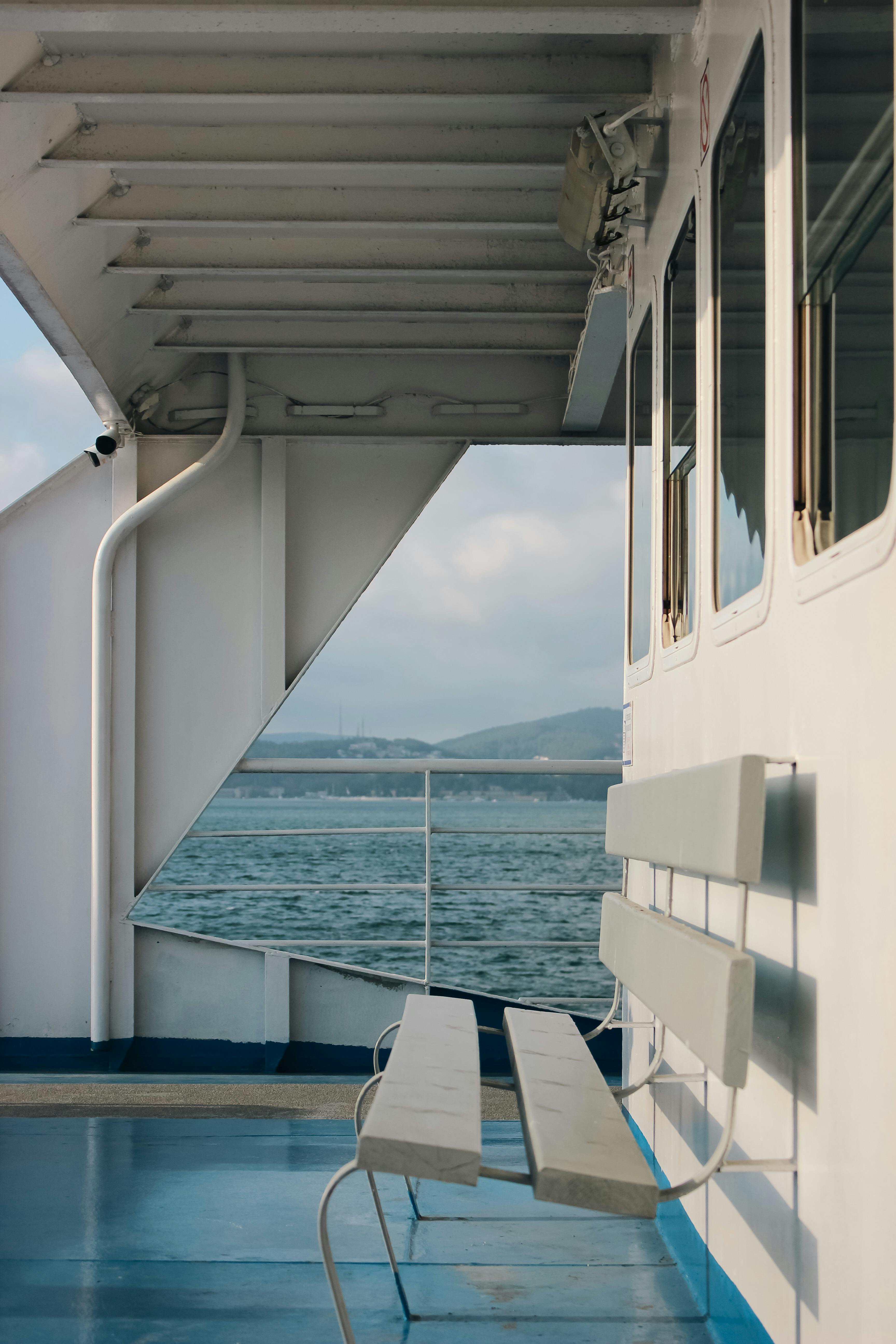 An empty bench on a ferry deck with sea and mountains in the background.