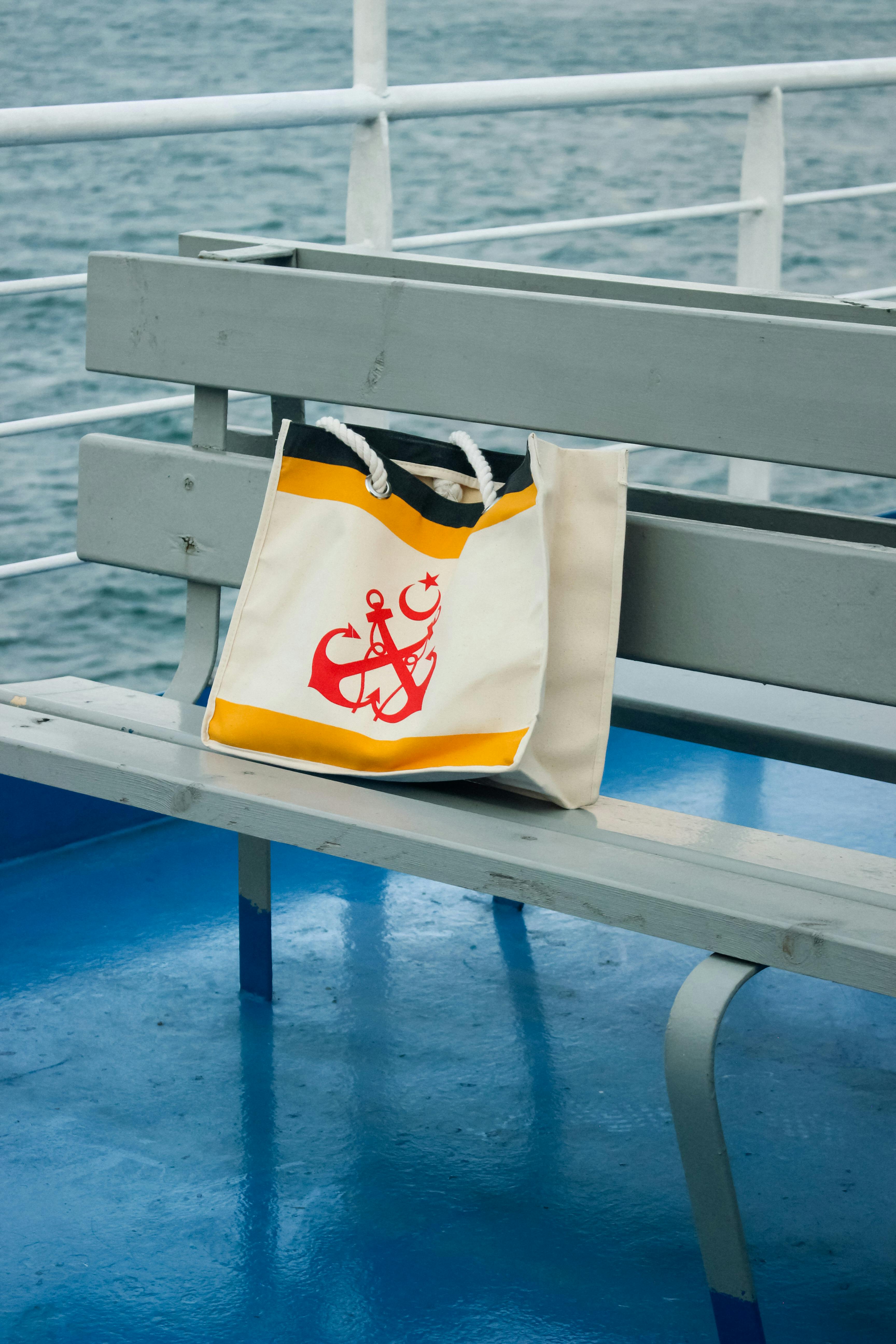 Free A stylish nautical themed beach bag placed on a ferry bench overlooking the ocean. Stock Photo