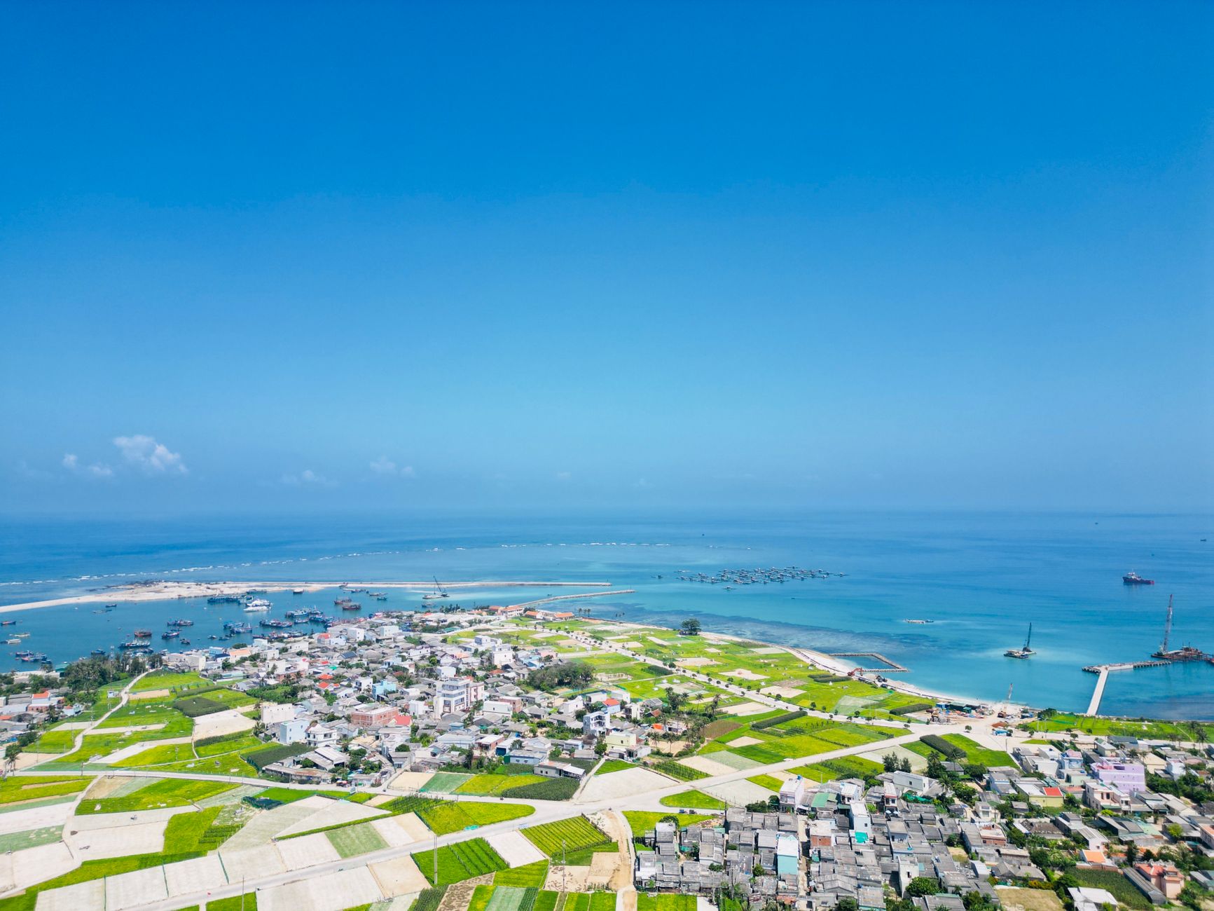 Aerial view capturing a vibrant coastal town with lush fields and a serene sea under clear blue skies.