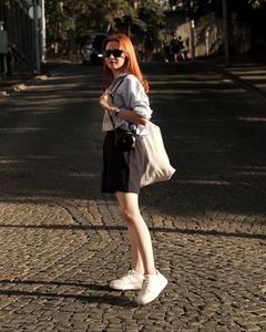 Red-haired woman walks on cobblestone street in Ankara, wearing sunglasses and casual outfit, showcasing urban fashion.