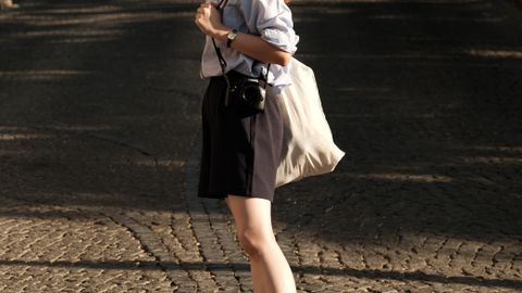 Red-haired woman walks on cobblestone street in Ankara, wearing sunglasses and casual outfit, showcasing urban fashion.