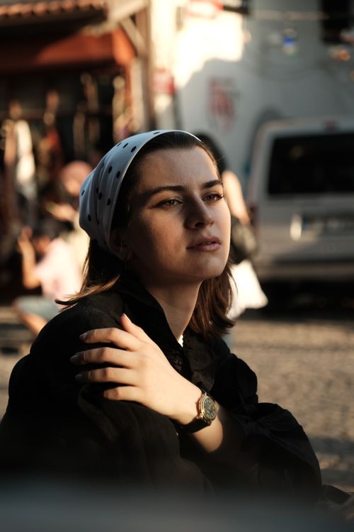 Free Woman in headscarf sitting on a city street, embracing sunlight with a thoughtful expression. Stock Photo