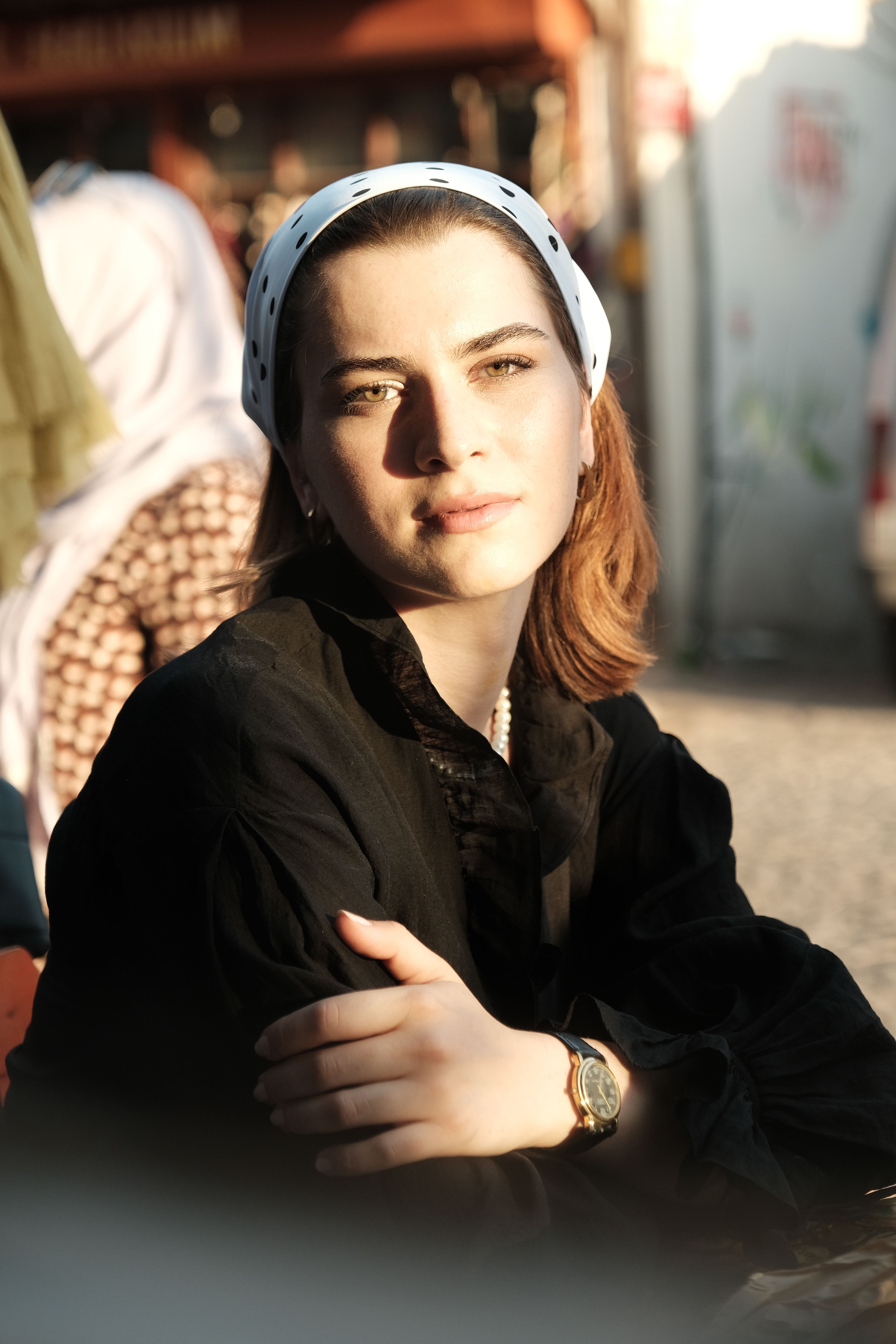 A serene portrait of a young woman sitting outdoors in urban sunlight, exuding elegance and style.