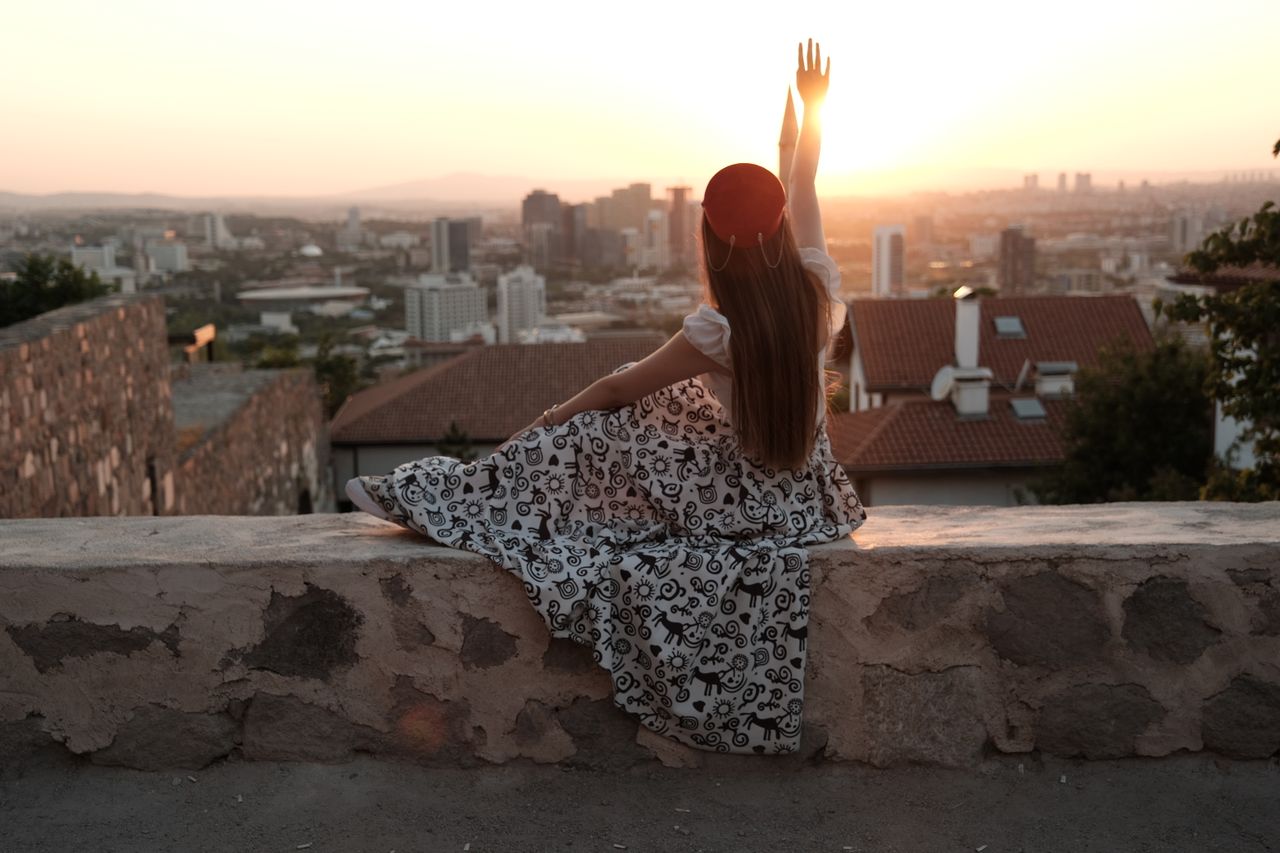 a young woman in a patterned dress enjoys a vibrant sunset from a city