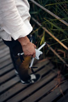 An adult holding a drone while standing on a wooden pathway surrounded by greenery.