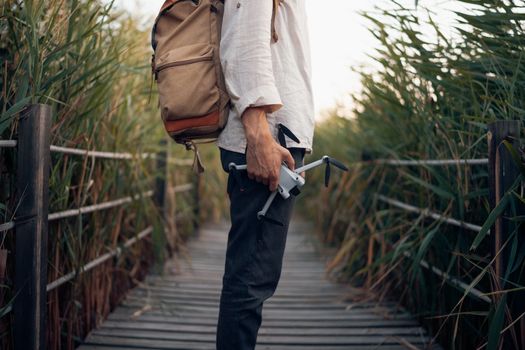 An adventurer with a backpack and drone on a boardwalk surrounded by reeds.