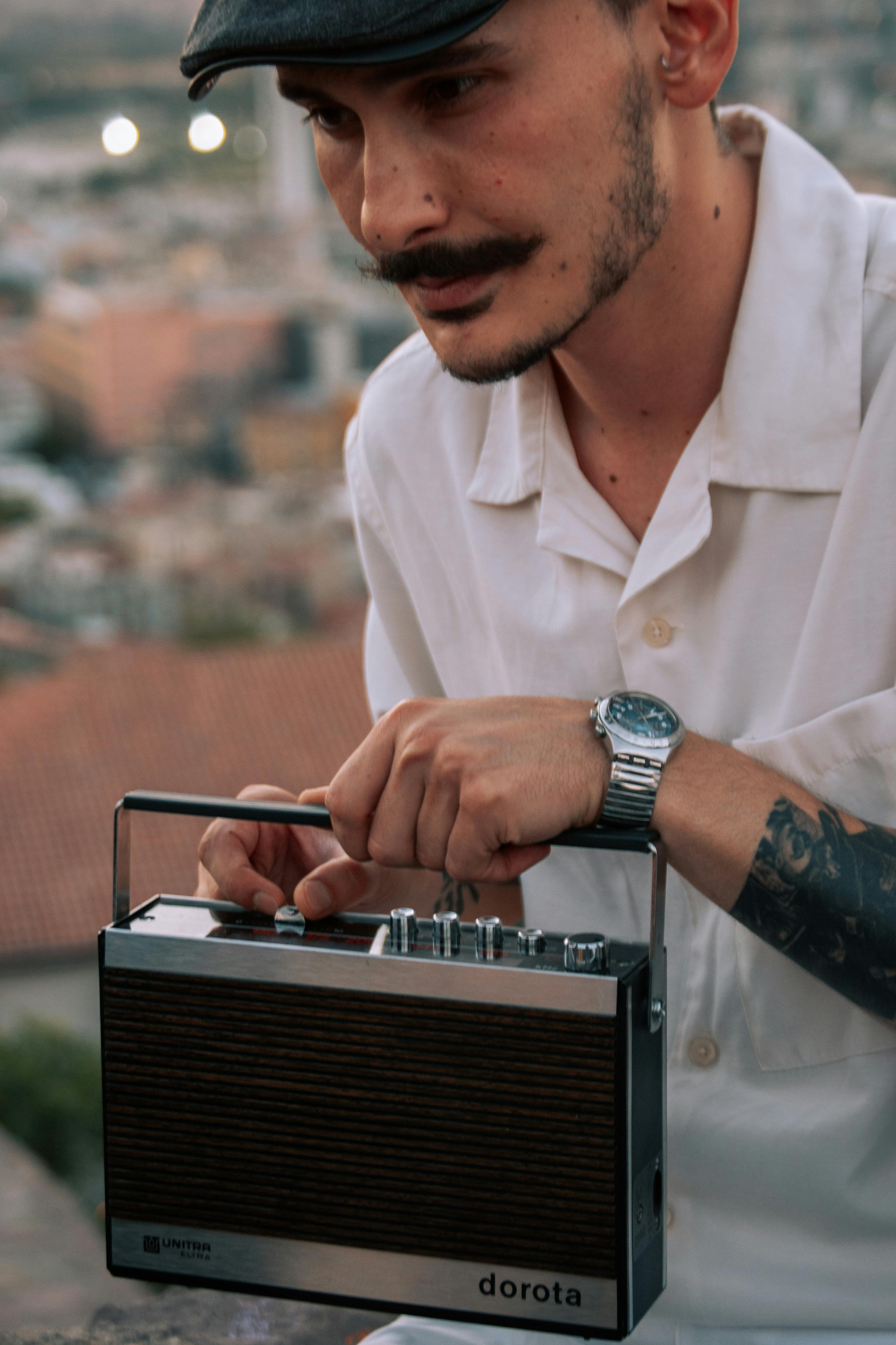 Man with mustache holding a vintage radio, embracing retro style outdoors.