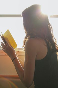 A woman sits by a sunlit window reading a book, surrounded by lens flare and warm sunbeams.. pexels, woman, sits