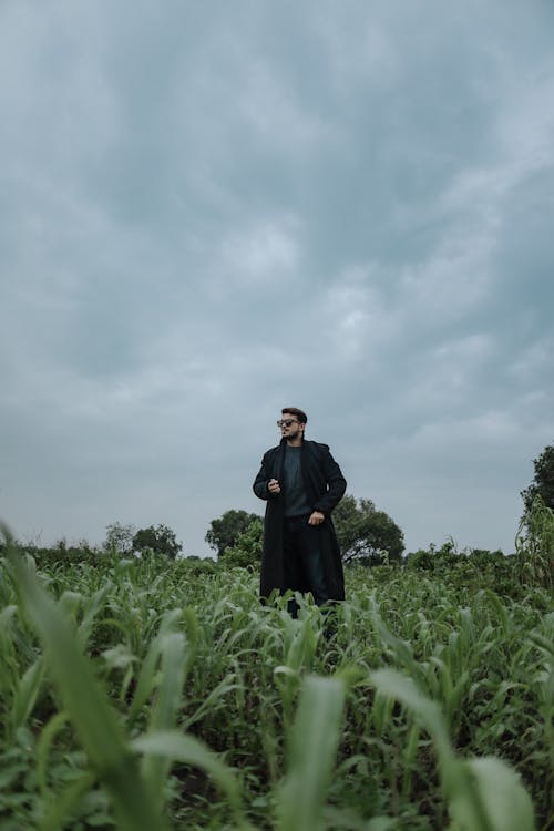 Young Man in Black Trench Coat Posing in a Field with a Cigarette