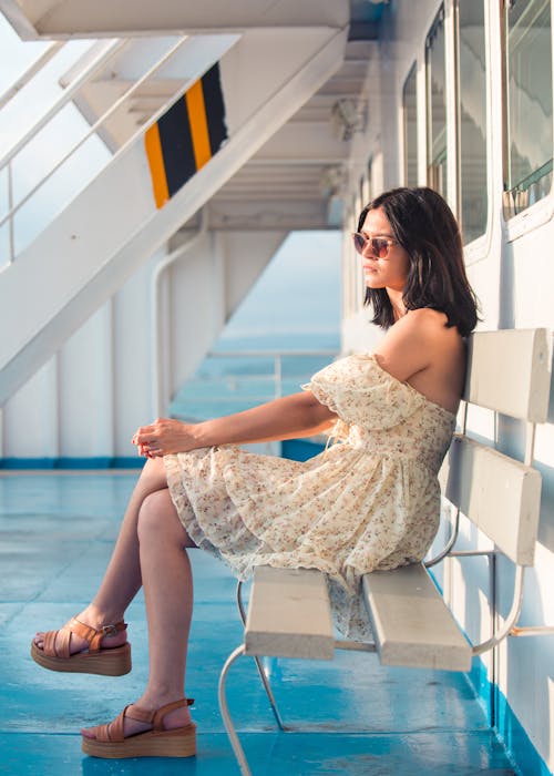 Woman in Floral Strapless Dress Sits on Bench at Ship Deck