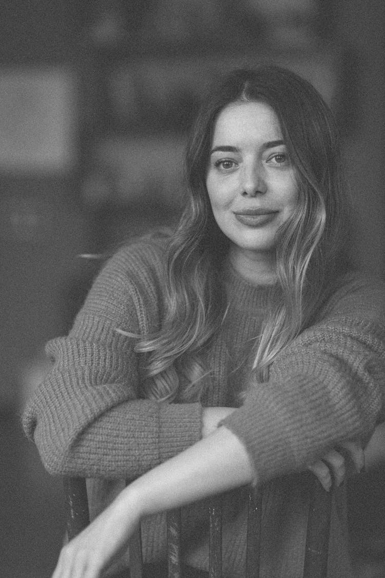 Black And White Portrait Of A Young Woman In Sweater Straddling A Chair