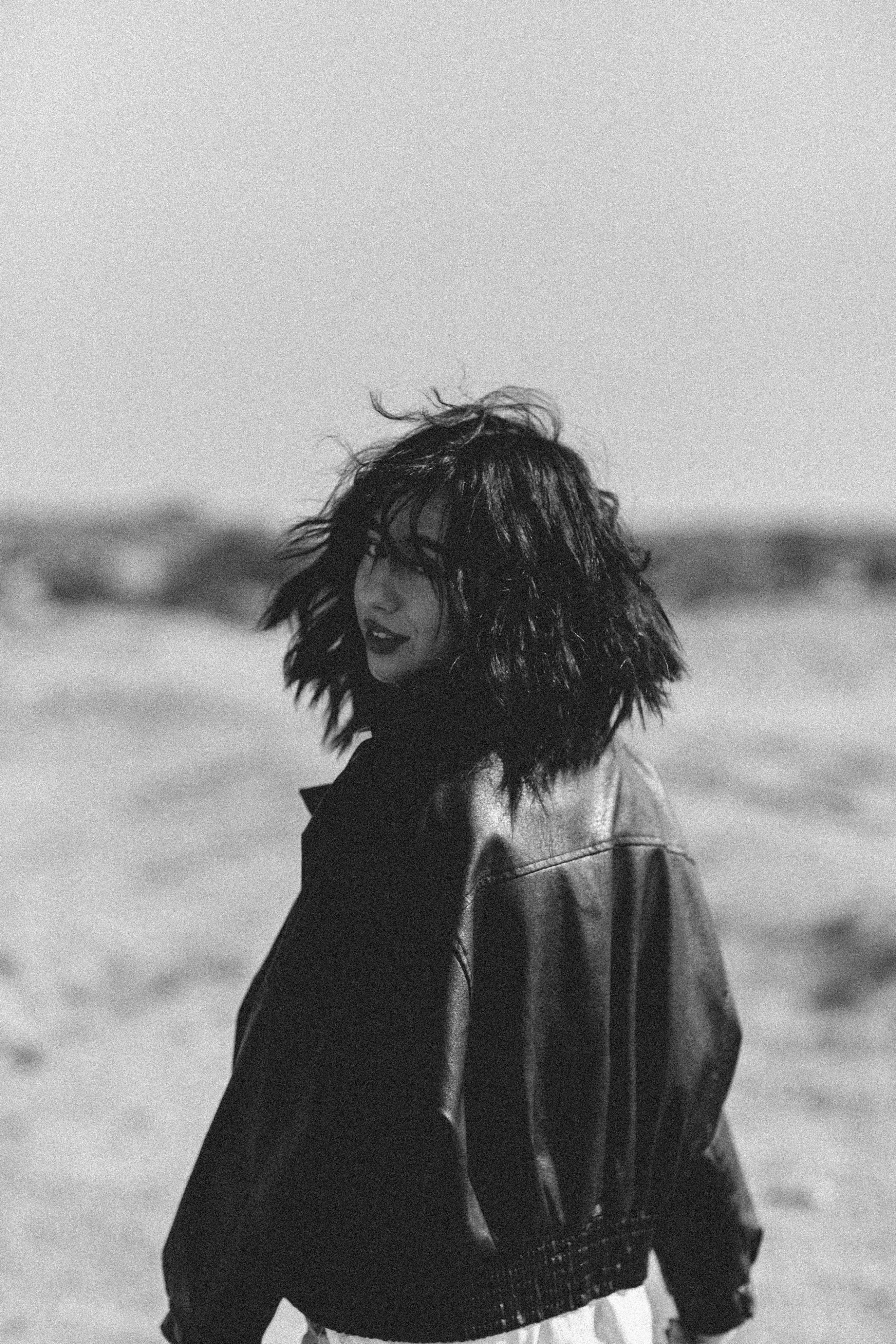 Black and white portrait of a young woman with wavy hair wearing a leather jacket outdoors.