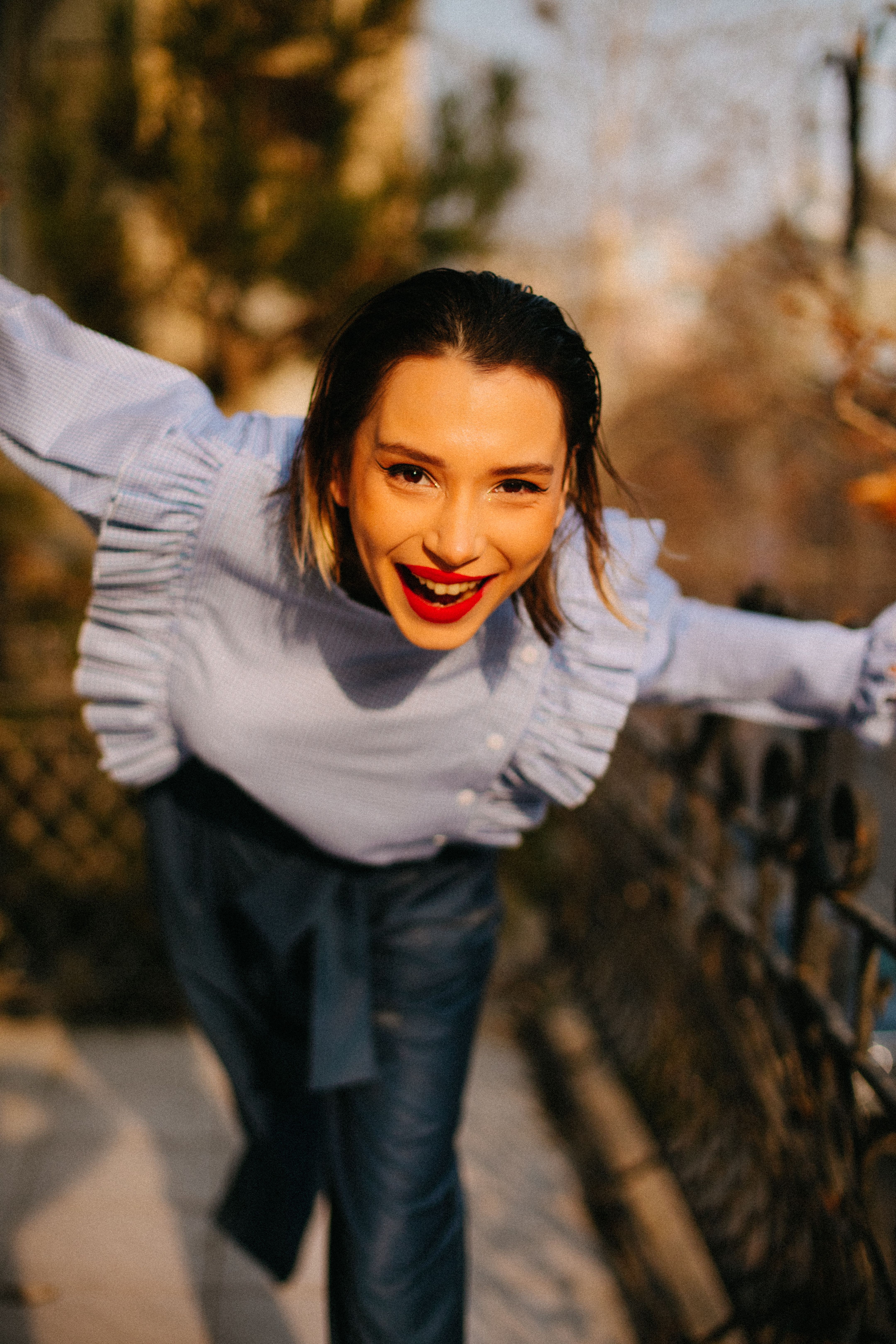Smiling woman in a stylish blouse enjoys a sunny day outside, exuding happiness.