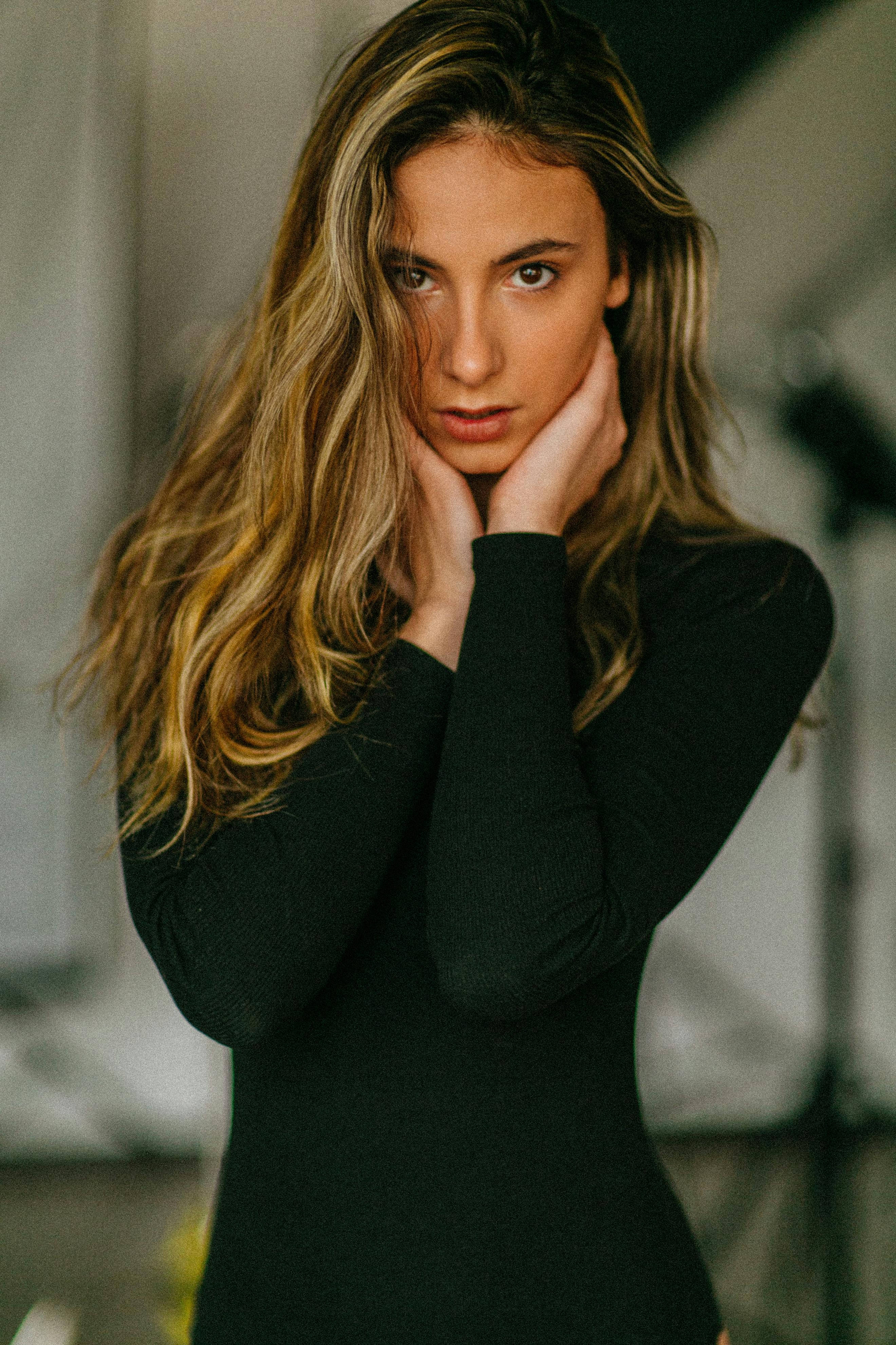 Portrait of a woman in a black dress with hands on neck, exuding elegance and sophistication.