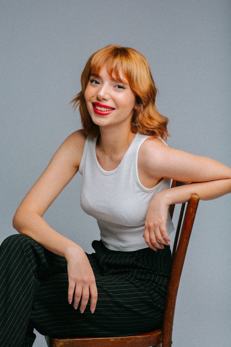 Studio Shot Of A Young Woman Sitting On A Chair And Smiling 