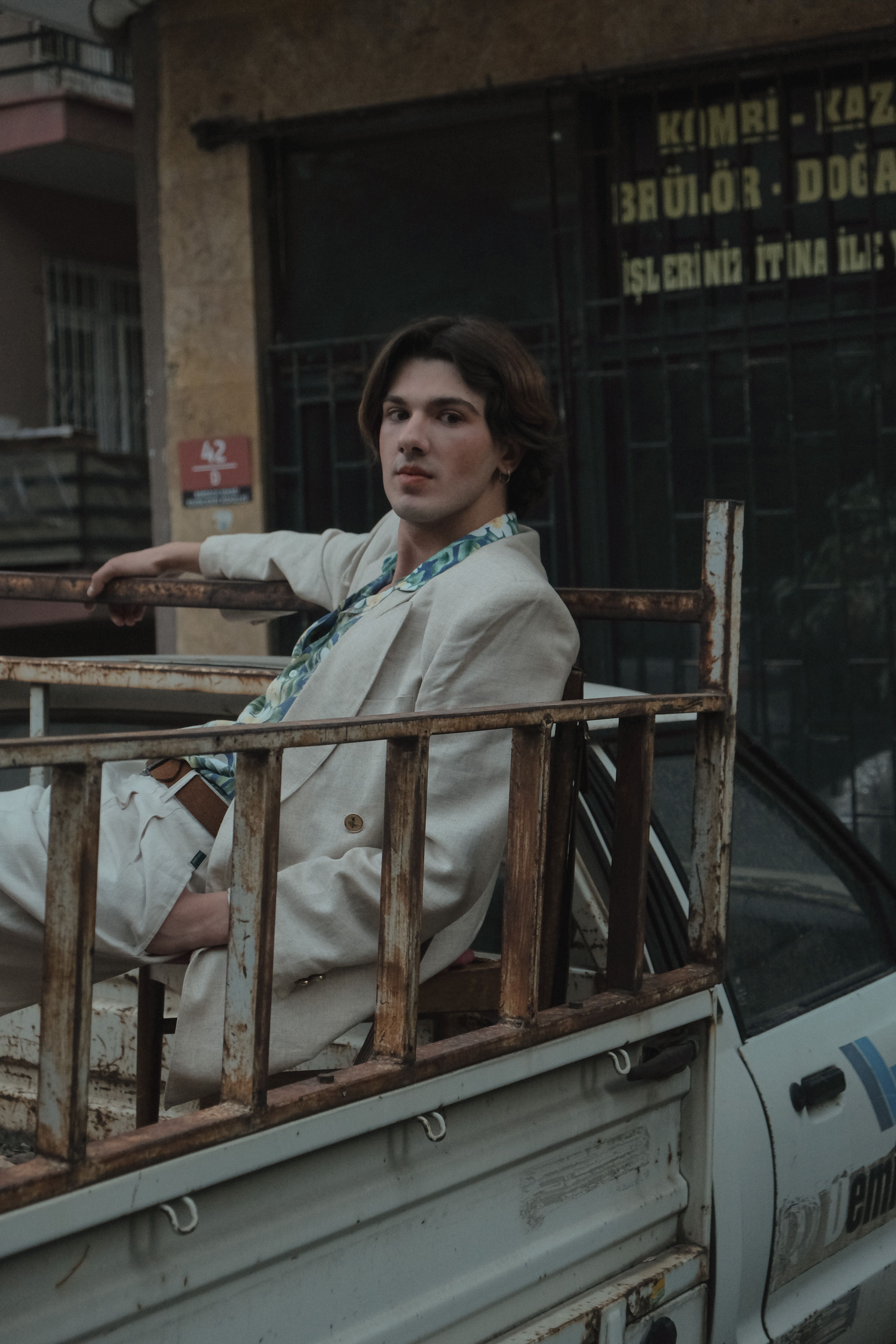 Young man in jacket sitting on a vintage vehicle in an urban setting, conveying modern fashion.