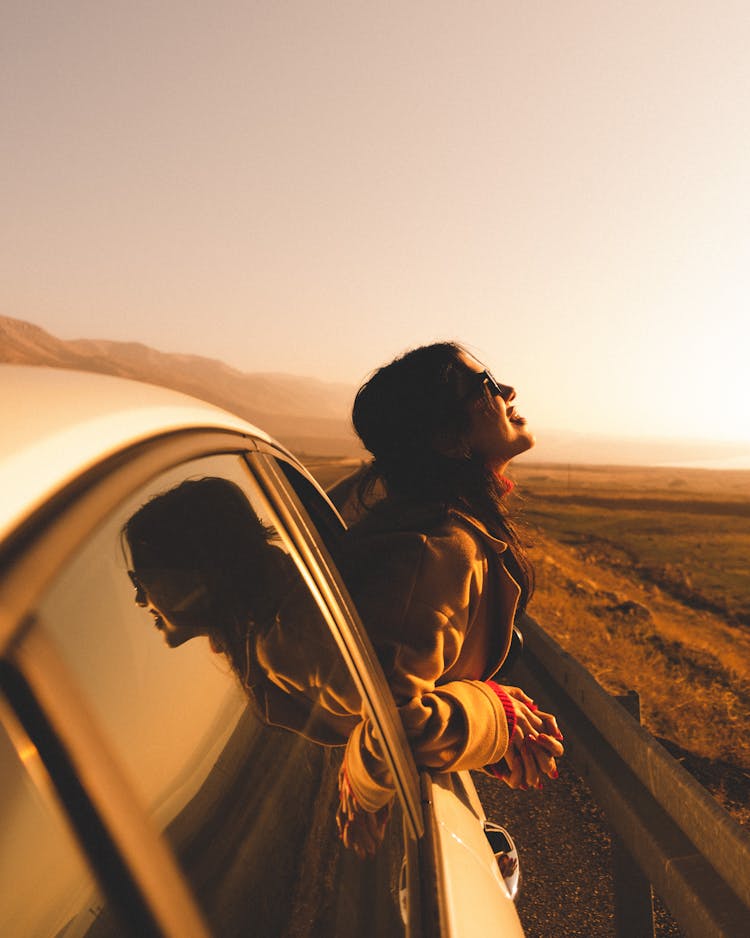 Woman In Car Window On Road At Sunset