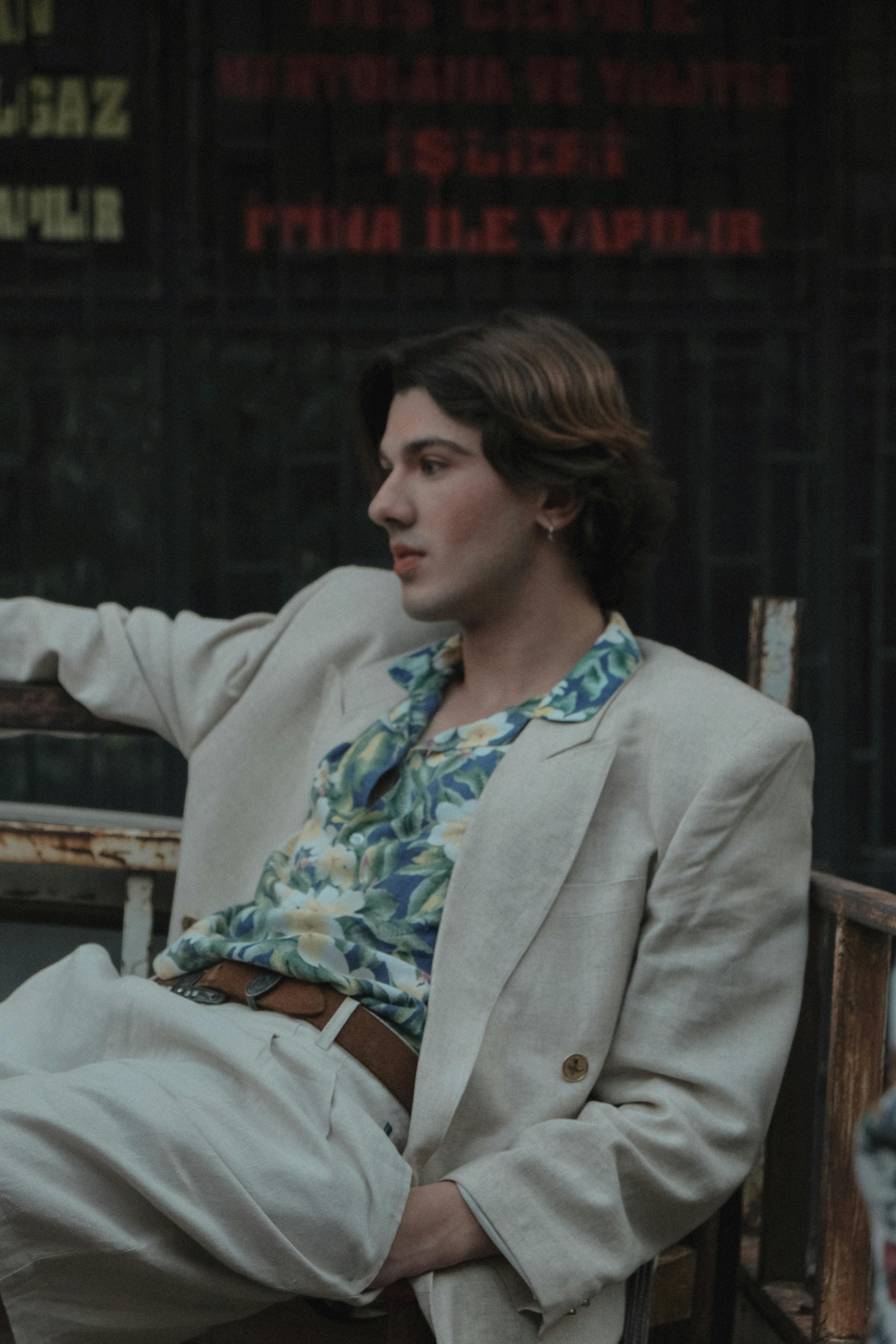 Fashionable young man in a beige suit sitting in an urban environment, exuding a relaxed vibe.