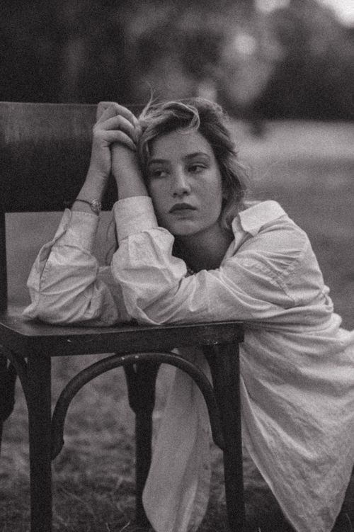 Free Black and white portrait of a young woman posing thoughtfully on a chair in a rural setting. Stock Photo