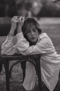 Black and white portrait of a woman leaning on a chair with eyes closed in an outdoor setting.