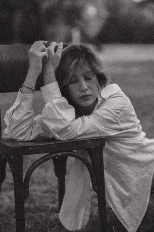 Free Black and white portrait of a woman leaning on a chair with eyes closed in an outdoor setting. Stock Photo