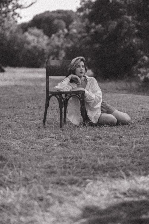 Free Black and white portrait of a woman sitting on grass outdoors with a chair. Stock Photo