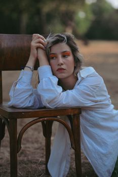 A serene portrait of a young woman in a white shirt resting on a chair outdoors during summer.