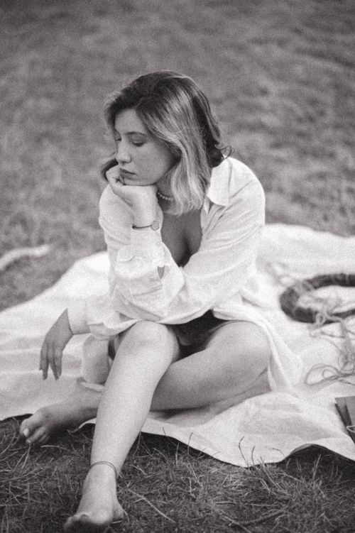 Free A woman sitting outdoors on a blanket, captured in a moody black and white portrait. Stock Photo