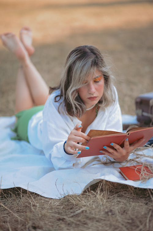 Young Woman Lying on a Blanket on the Grass and Reading a Book 