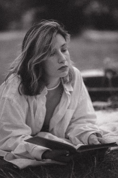 Free Adult woman reading a book lying on a blanket outdoors in a serene setting. Stock Photo