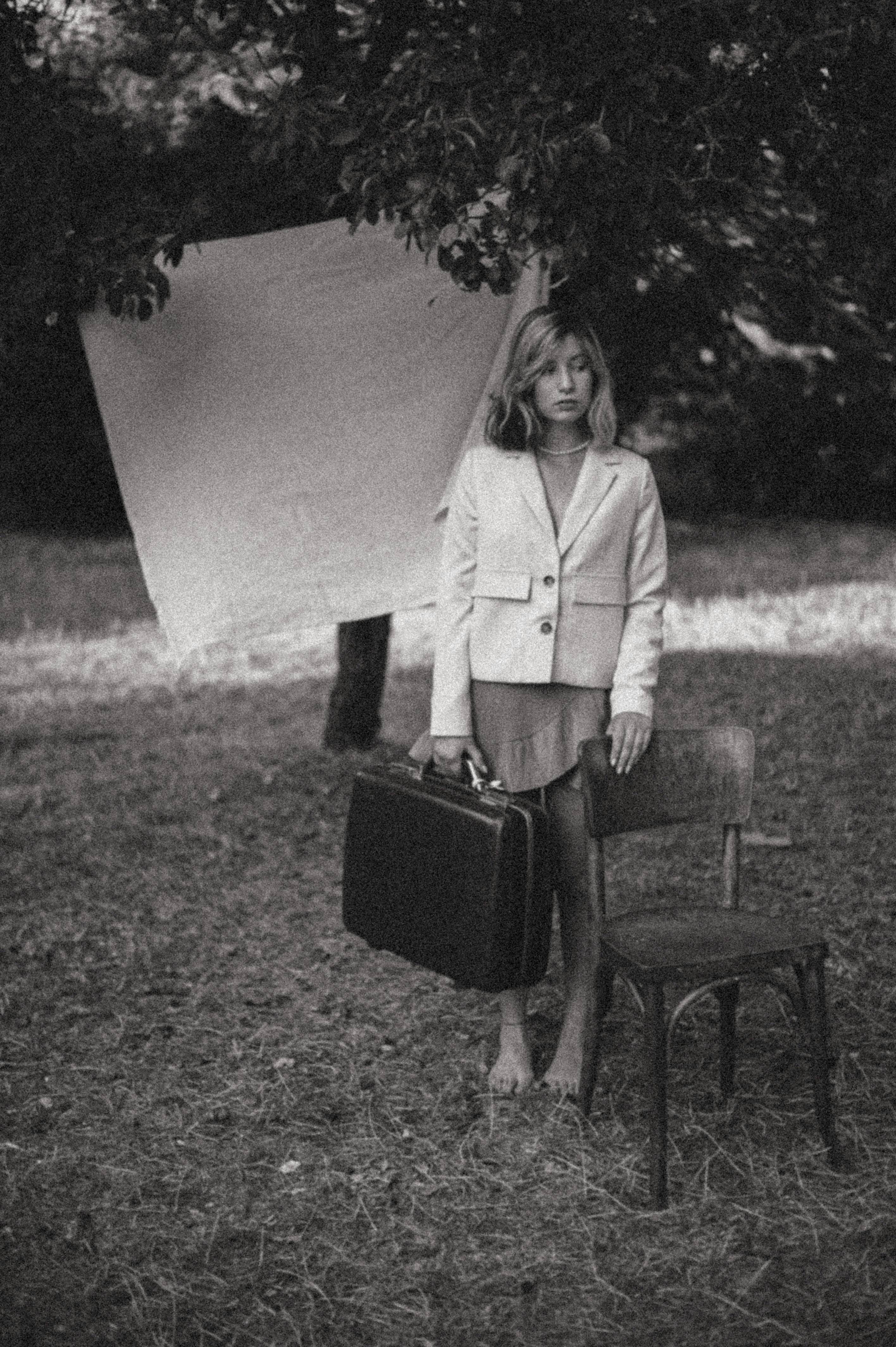 Model in a Blazer and Tulip Skirt with Her Hand Rested on a Chair Holding a  Suitcase Posing Under the Tree · Free Stock Photo