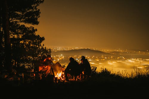 Silhouette of People Sitting by a Capfire, and Yellow Illuminated Landscape by Night