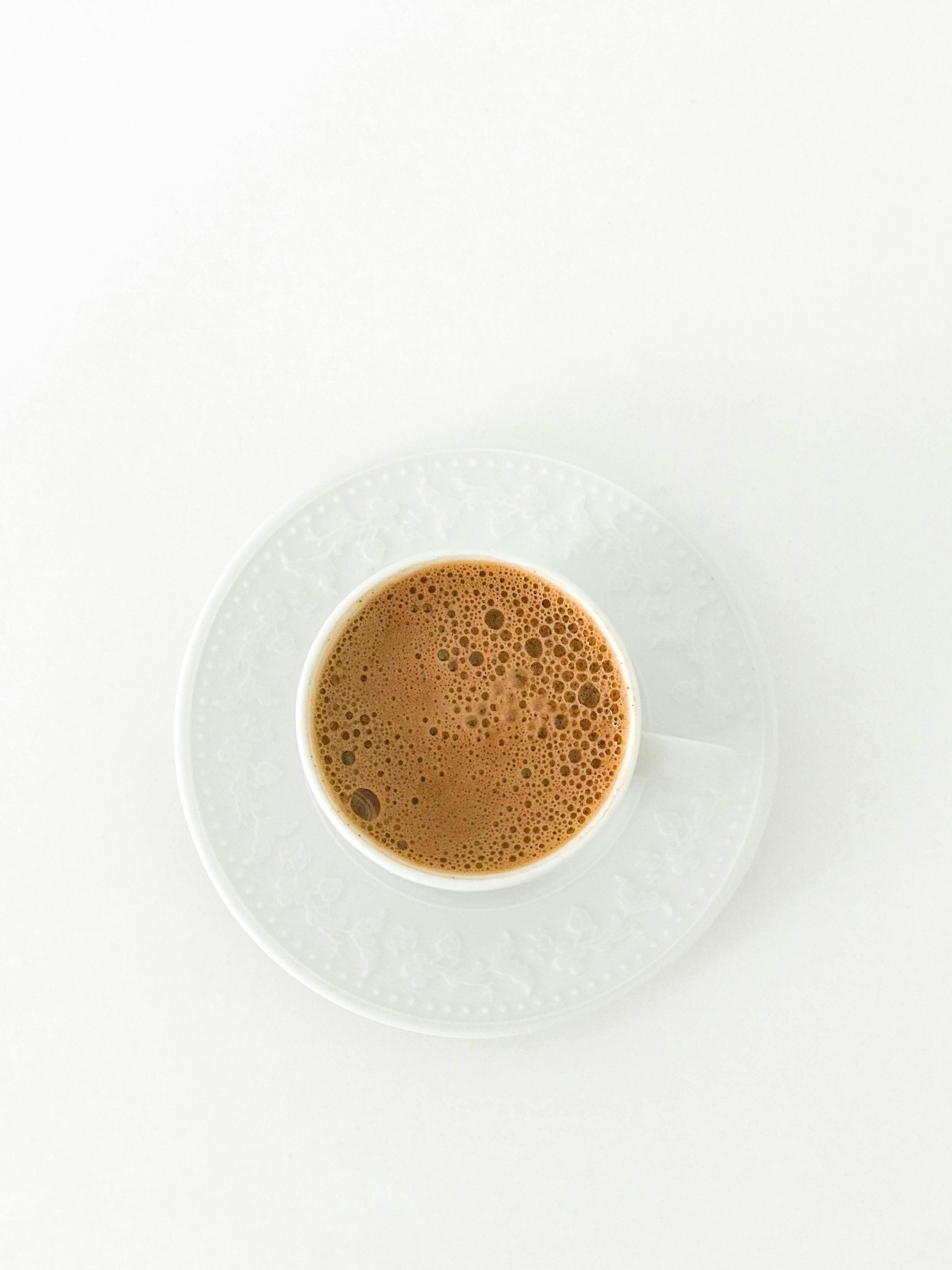 Minimalist top view of a frothy Turkish coffee in a white cup and saucer on a white background.