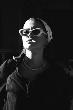 A stylish woman wearing sunglasses and pearls in a dramatic black and white portrait.