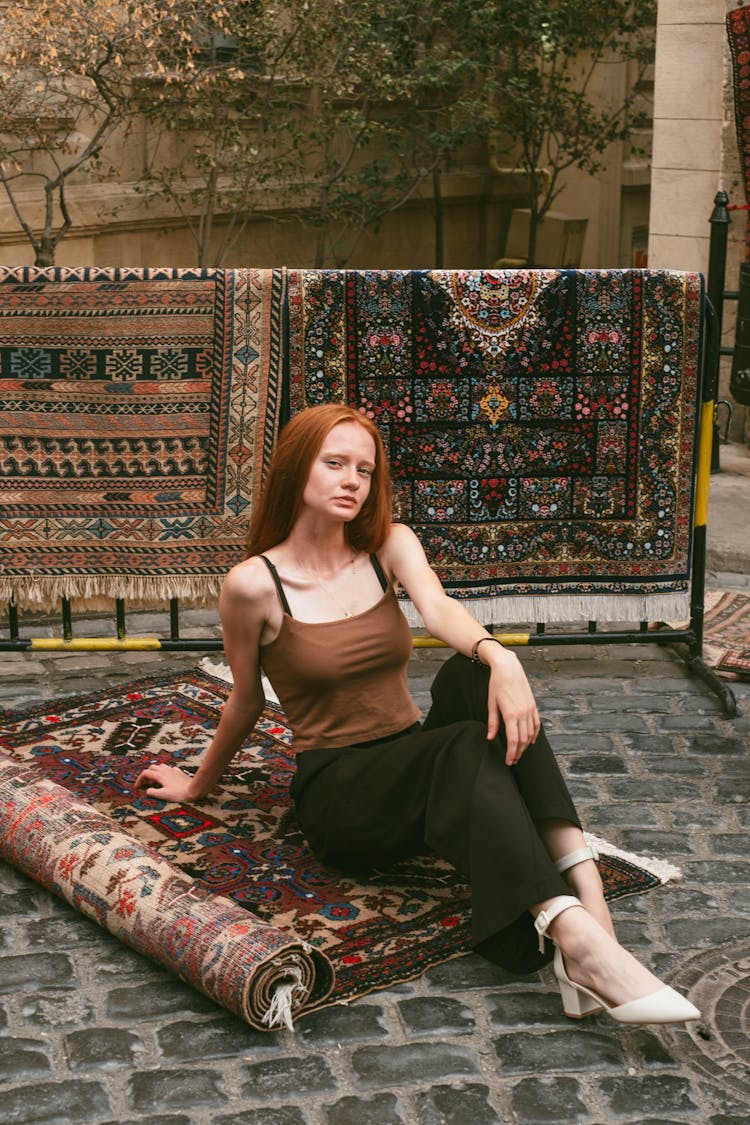 Young Woman Sitting On The Ground With Rugs With Traditional Oriental Patterns 