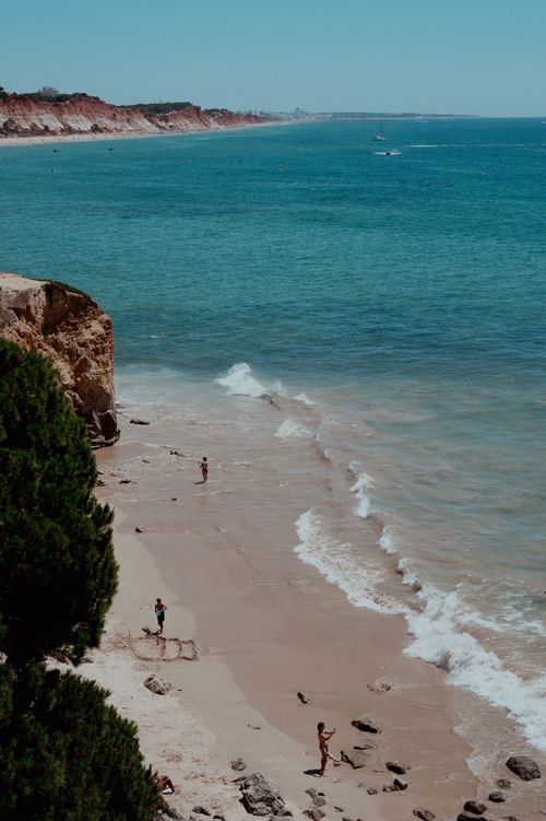 Free Relaxing scenic view of a sunny beach with cliffs, ocean waves, and people enjoying the coast. Stock Photo