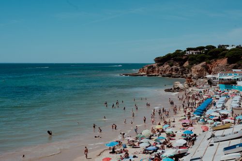 Free Crowded beach scene with colorful umbrellas and people enjoying a sunny day by the ocean. Stock Photo