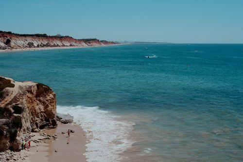 Free A captivating view of the coast with cliffs, ocean waves, and a distant motorboat under clear skies. Stock Photo